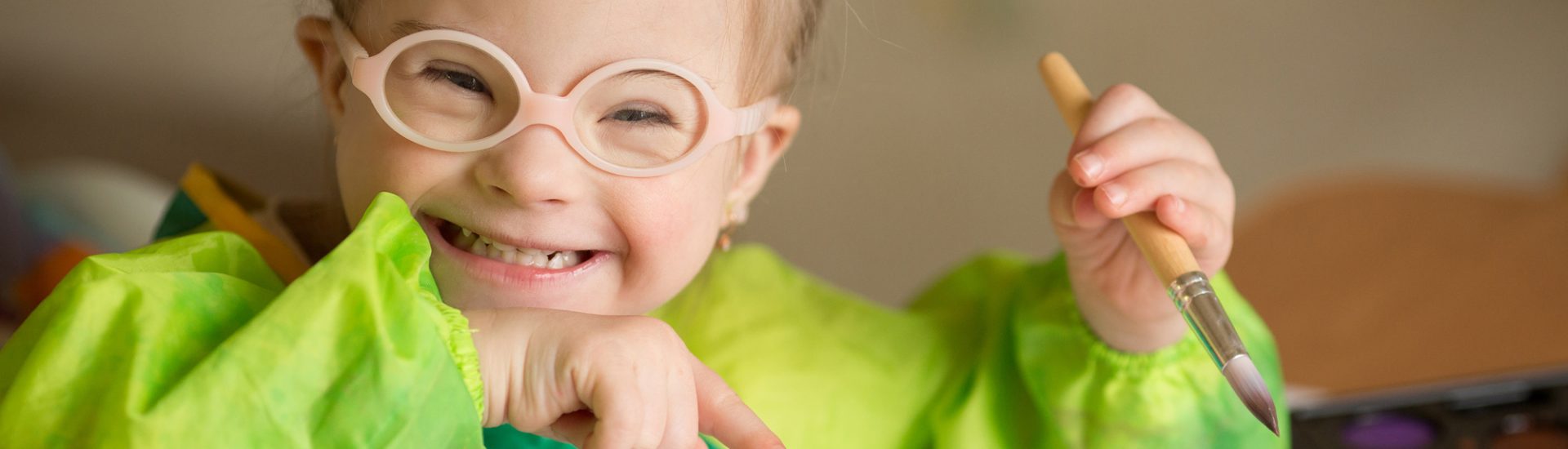 Child wearing glasses laughing while holding a paint brush