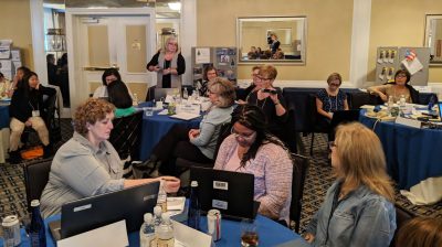 Workshop attendees sitting at their individual tables passing around a microphone to discuss a topic