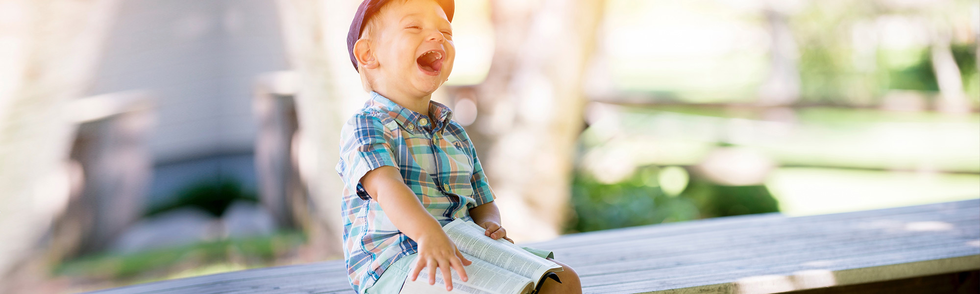 Young, disabled boy sitting on a bench laughing boisterously while reading a book