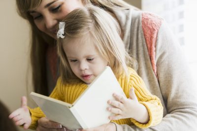 Young girl reading a book while sitting on a woman's lap